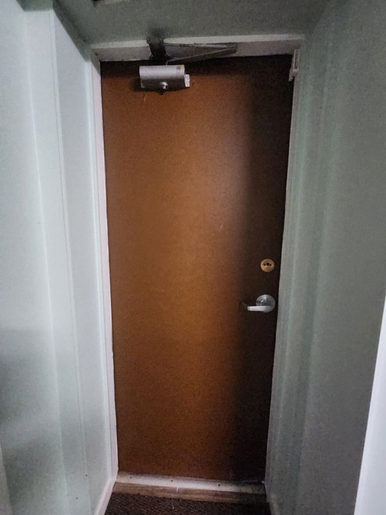 Brown condo corridor door with an overhead door closer, lever handle and key cylinder