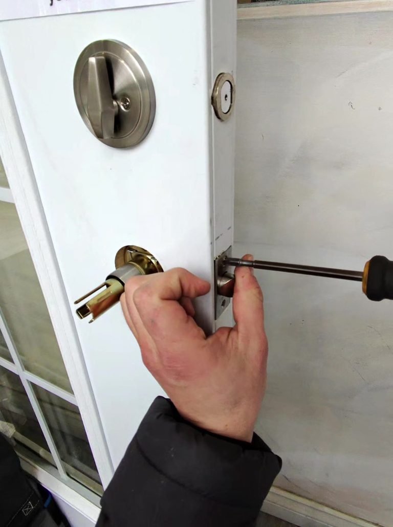 Satin nickel deadbolt and knob being installed on the glazed lobby entry door of a hotel