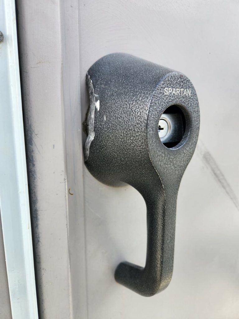 Black Spartan T-handle lock with key cylinder mounted on a grey steel gate